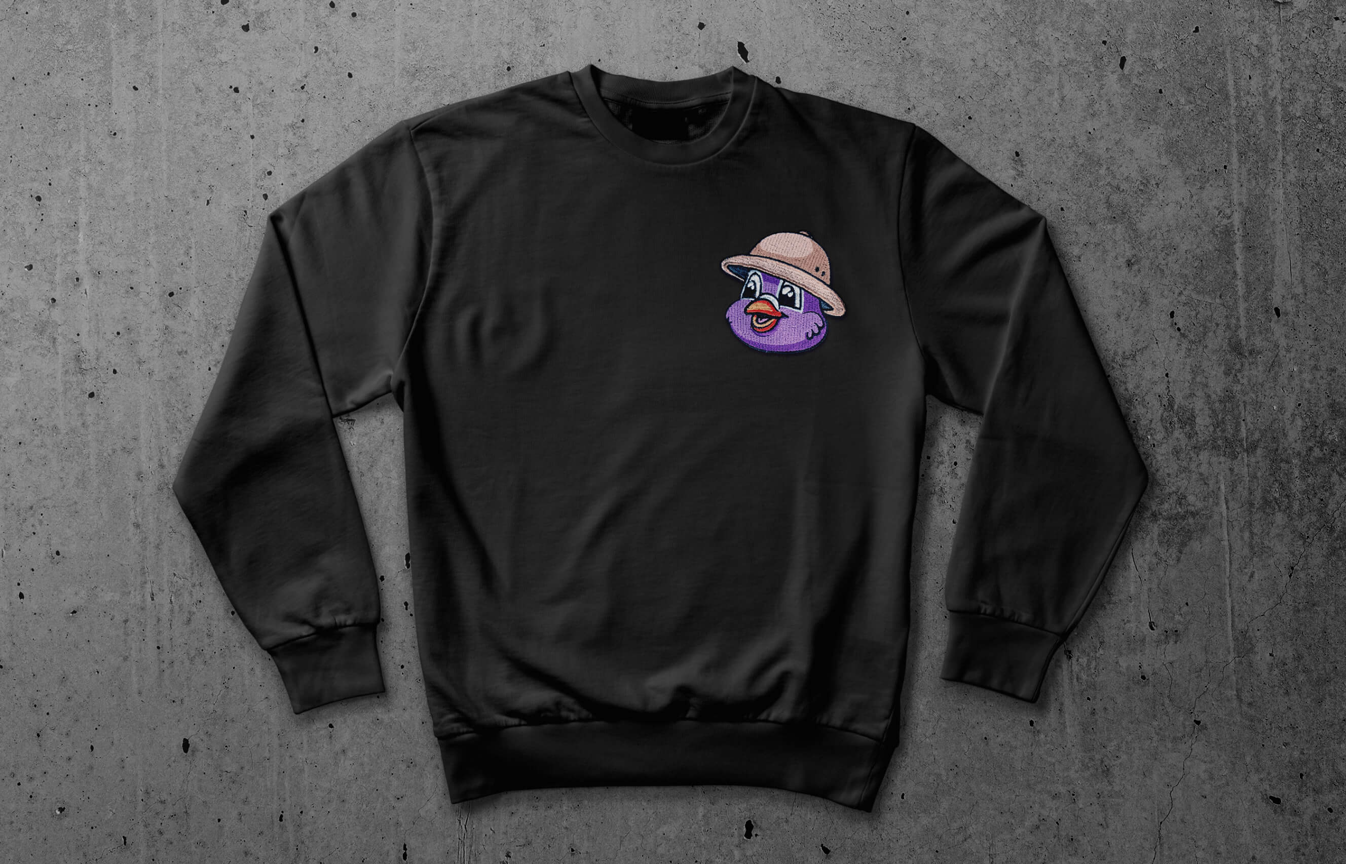 Sweater sitting on concrete with an embroidered patch of Pip's head with a safari hat on the left breast.