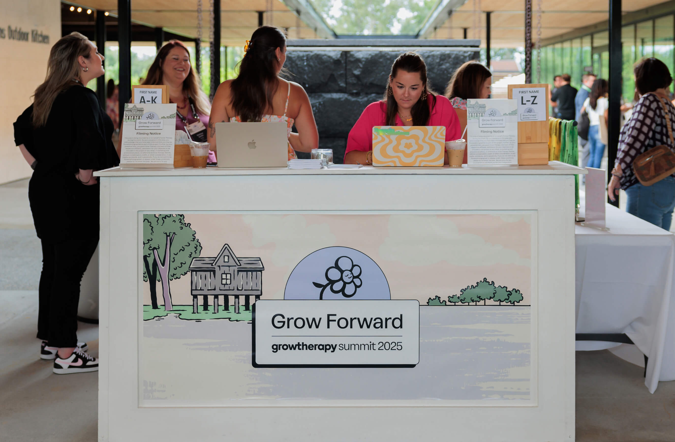 Semi-outdoor entryway to the Grow Forward summit. A woman behind a laptop waits at the welcome desk. A banner with illustrated nature scenery hangs in front with the Grow Forward logo on top of it.