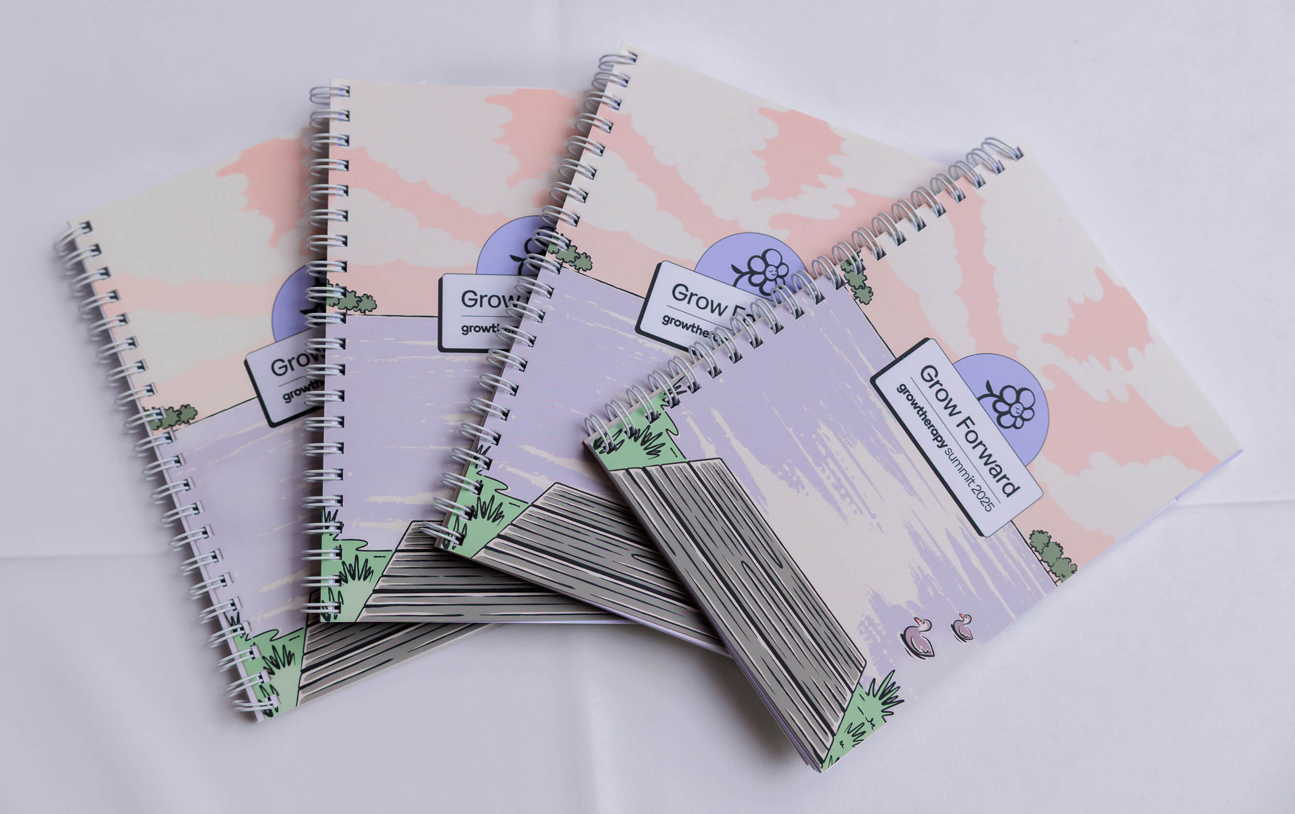 A notebook with illustrated nature scenery and the Grow Forward logo sits on a while tablecloth.