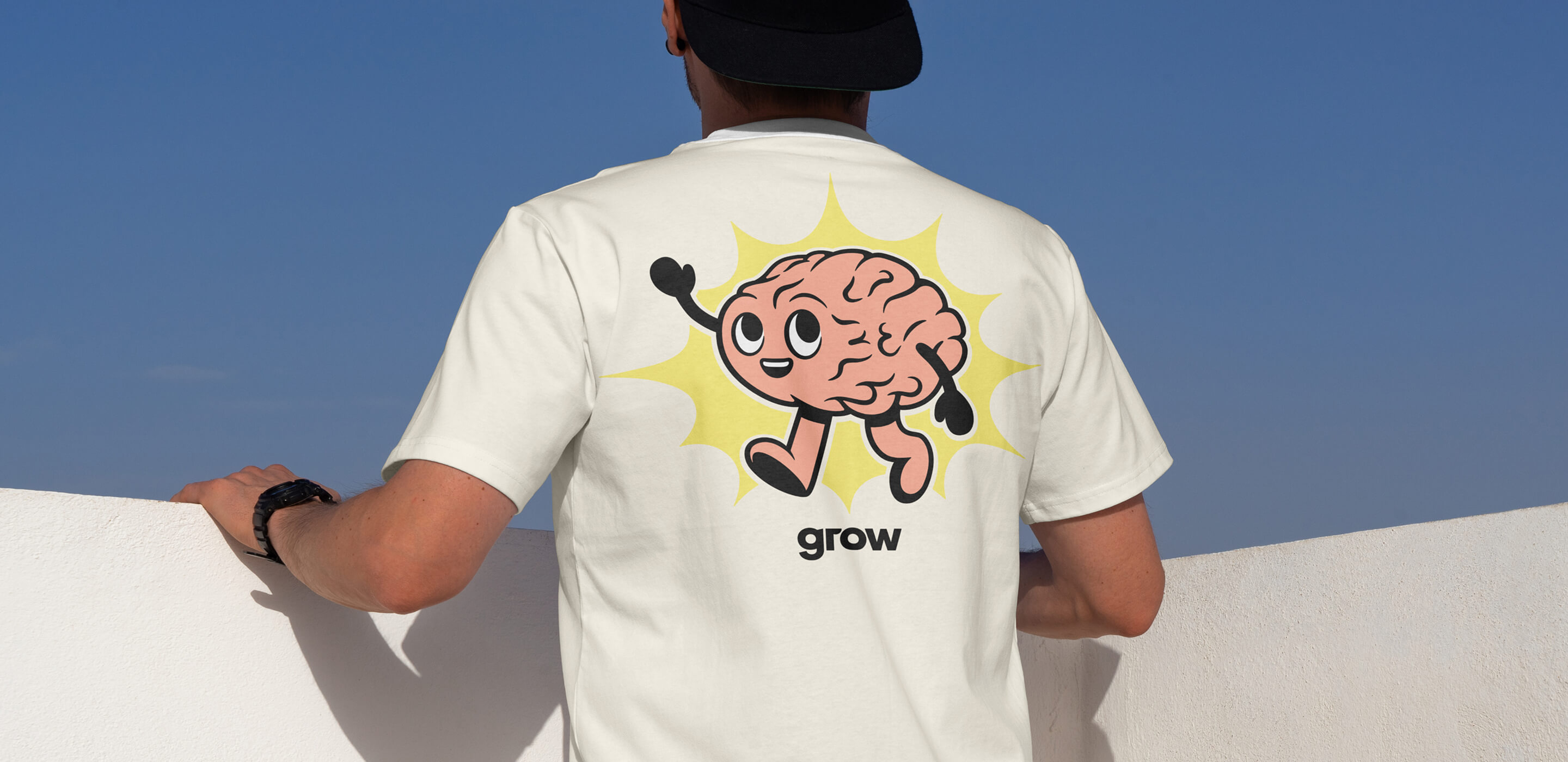 Photo of a person's back. They are wearing a white shirt with a playful brain character waving. It's the Neurodivergent ERG logo.