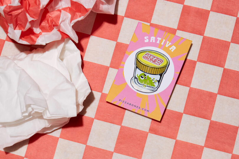 Photo of Sativa pin. The background is checkered red and white, and there's a crumpled napkin nearby.